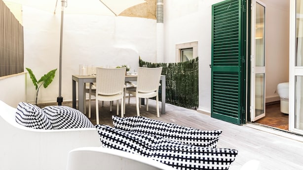 A modern outdoor seating area with a table and chairs, a large umbrella, and a sofa with patterned cushions.