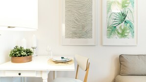 A dining area with a white table, a wooden side table with candles, and two framed artworks on the wall.