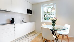 A modern kitchen with white cabinets, a microwave, and a coffee maker. There is a dining table with chairs and a vase of flowers. - Cord04 Blue House Apartment 4 Parking + Super Central (Porto)