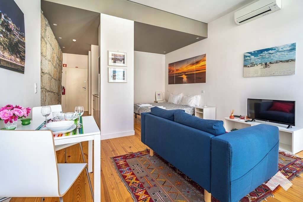 A modern living room with a blue sofa, a dining table with chairs, and a TV.