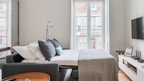 Hotellihuone, jossa on sänky, sohva, televisio, työpöytä ja ikkuna, josta on näkymä parvekkeelle.