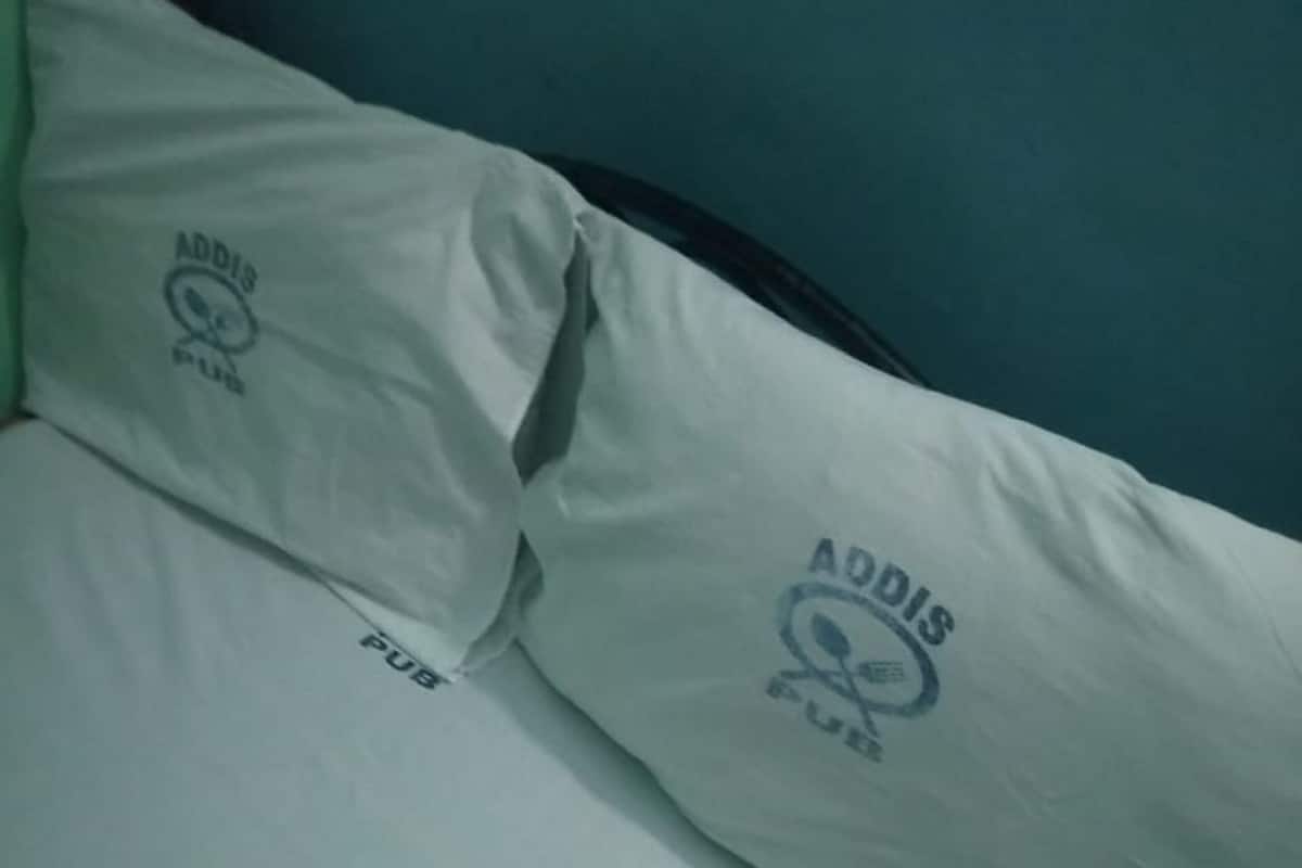 A bed with two pillows, each featuring the logo "Addis Pub."