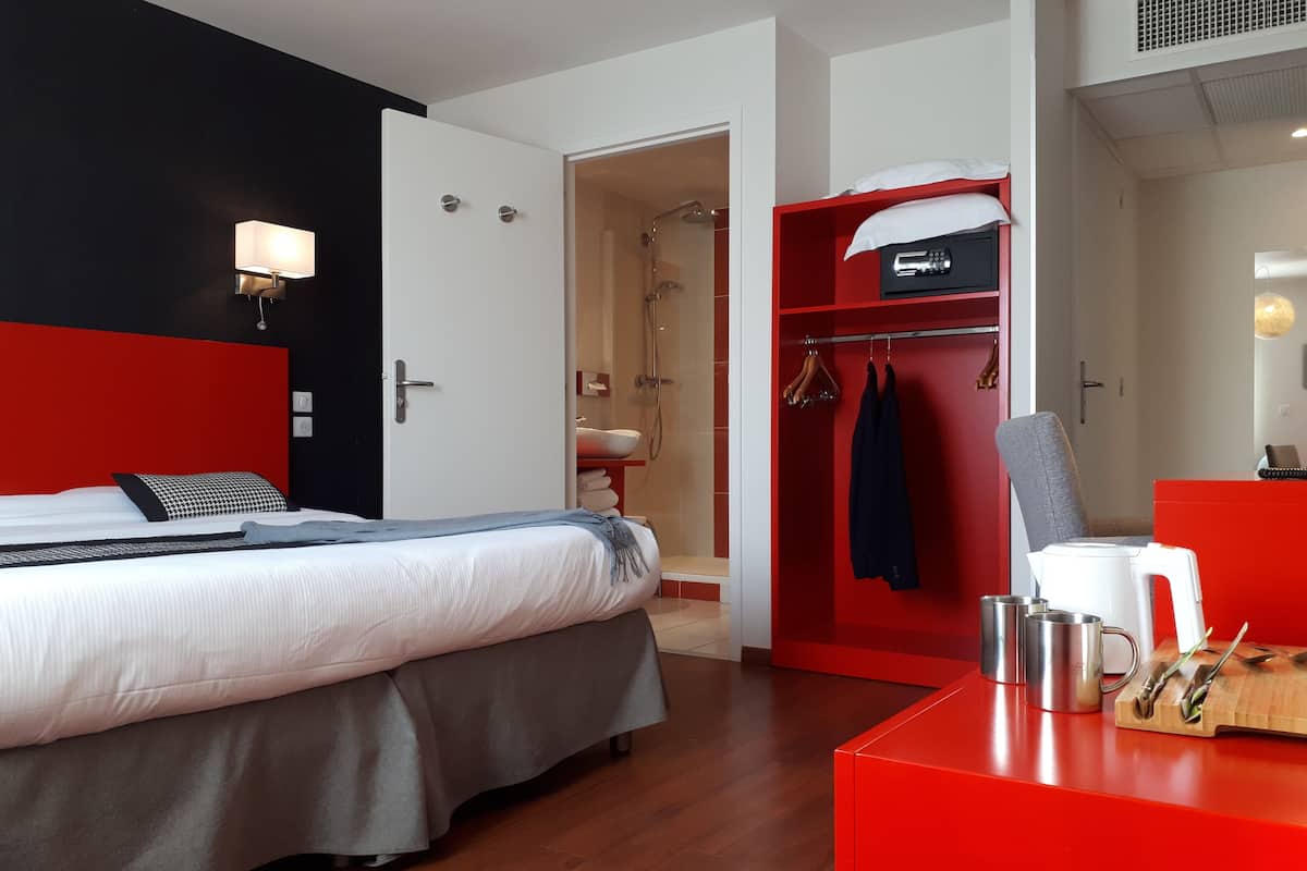 Een hotelkamer met een bed, een rode garderobe, een bureau met een mok en een mes, en een douche.