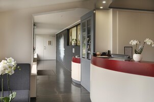 Un área de recepción con mostrador, una sala de espera con sofá y una planta en maceta.