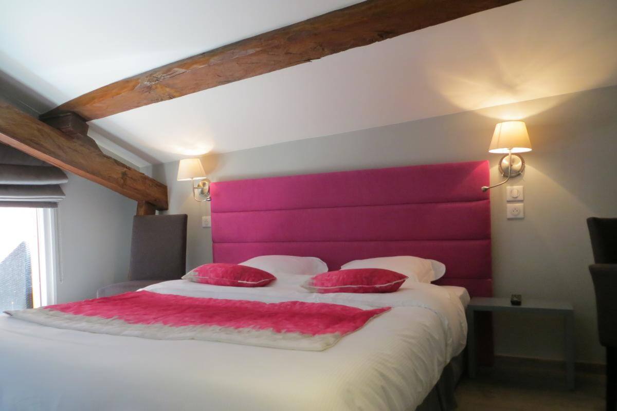 Een slaapkamer met een groot bed, twee bedlampen en een houten balk in het plafond.
