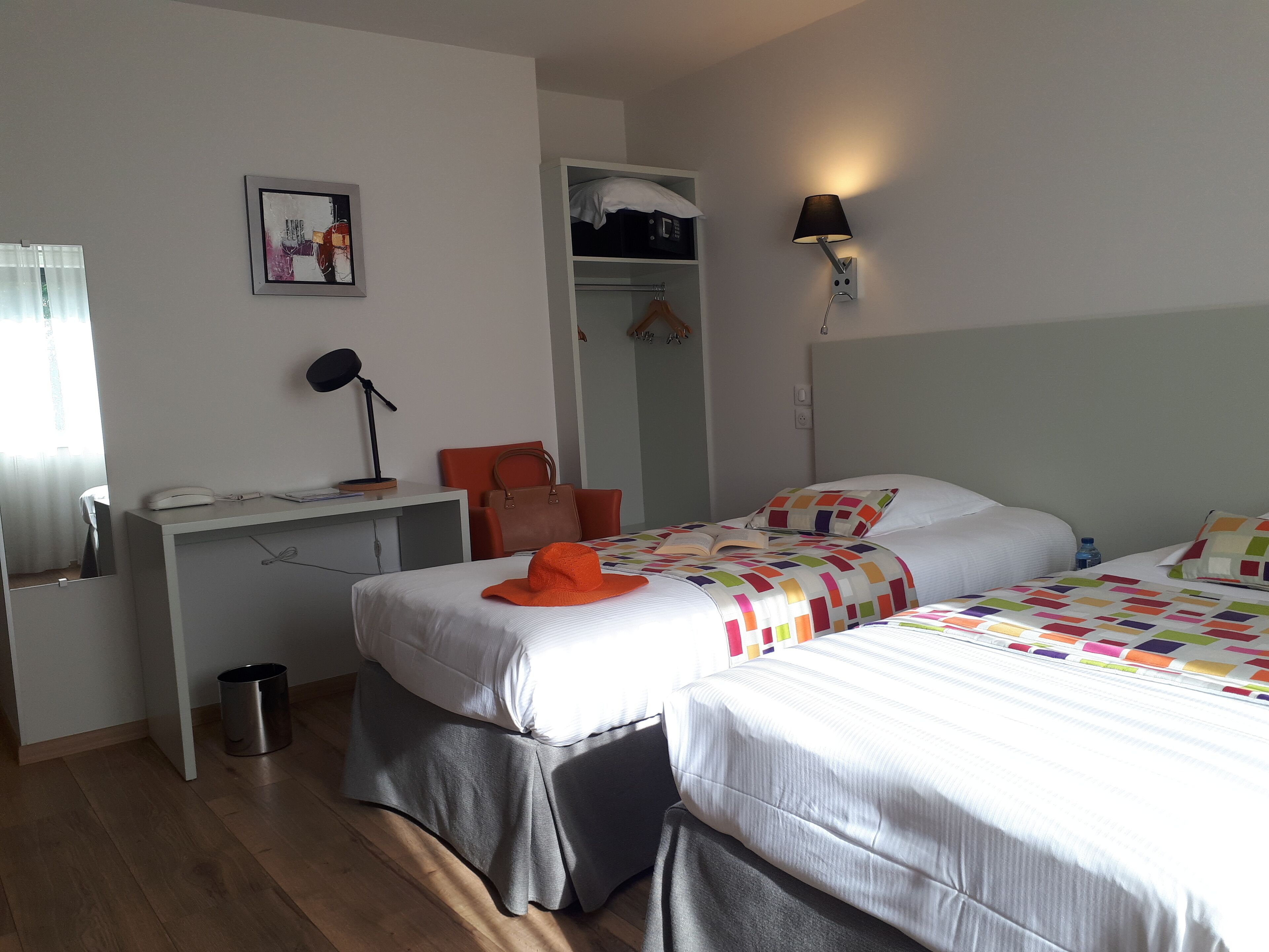 Et hotelværelse med to senge, et skrivebord med lampe, et garderobeskab og en lille skraldespand.