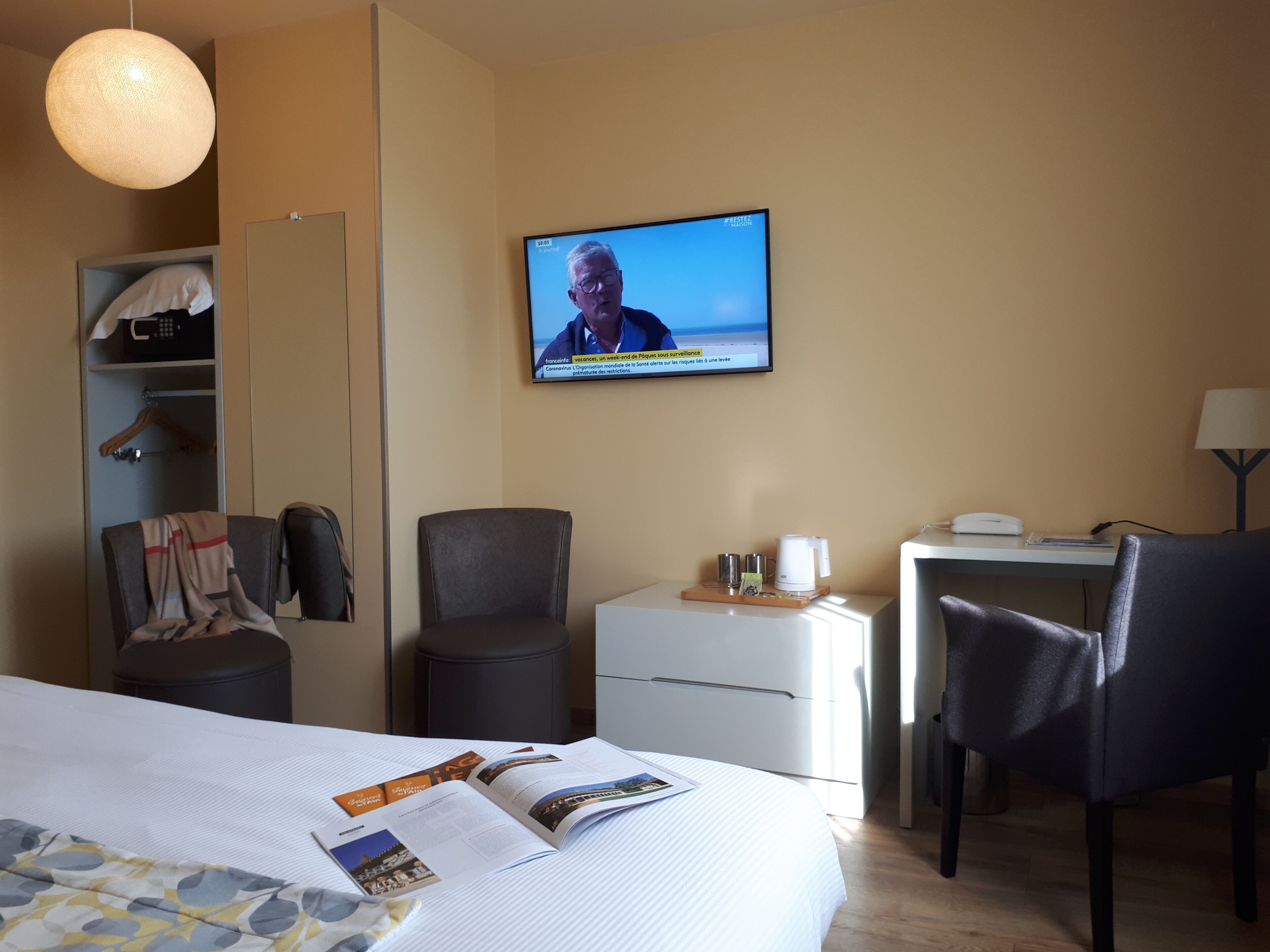 A hotel room with a bed, a desk, a chair, a TV, and a wardrobe.