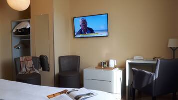 A hotel room with a bed, a desk, a chair, a TV, and a wardrobe.