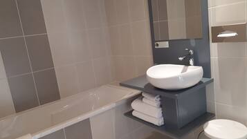 Uma casa de banho moderna com lavatório branco, espelho e um pequeno banquinho.