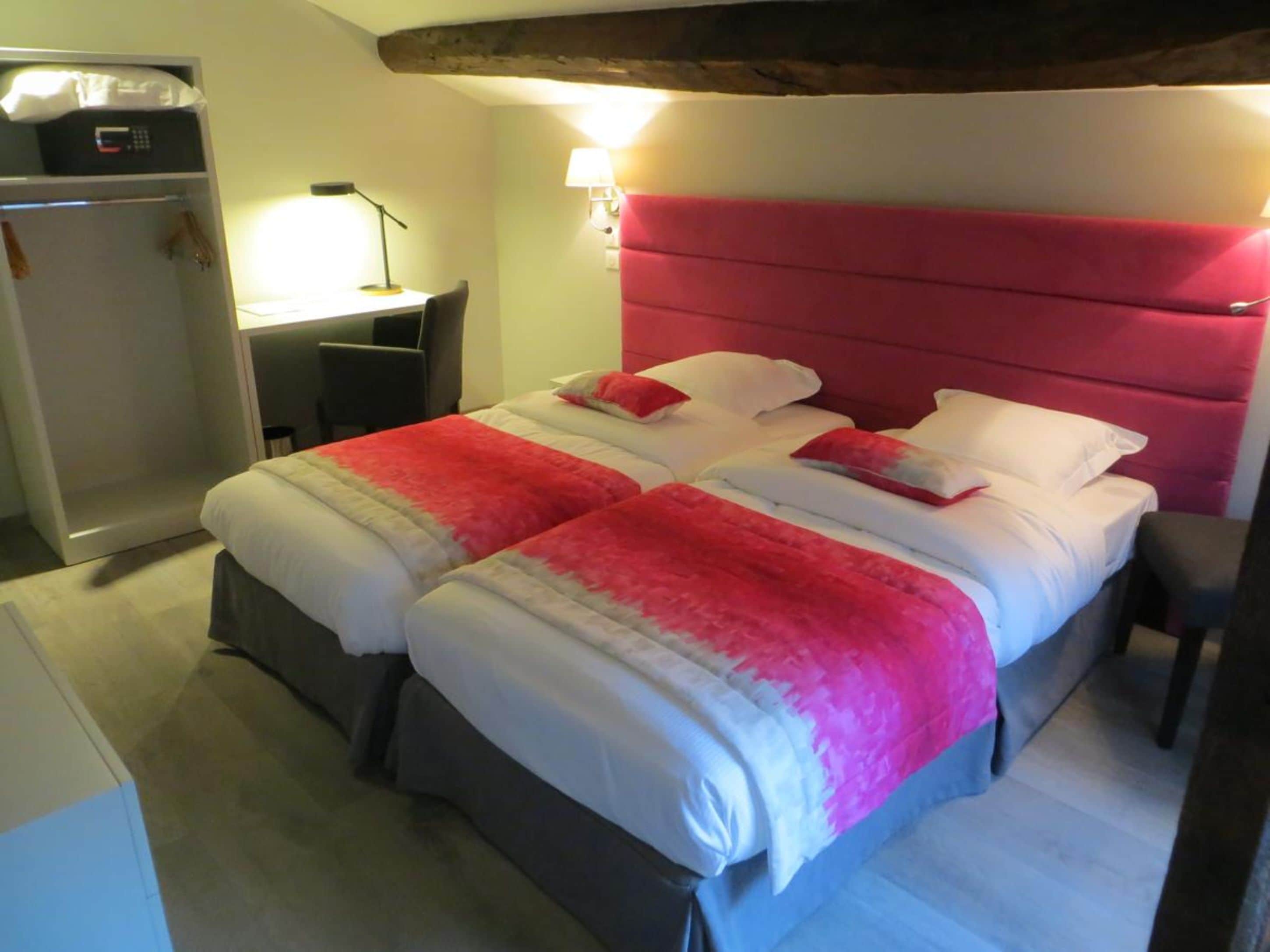 A double bed with a red headboard, a desk with a lamp, and a wardrobe.