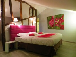Un dormitorio con una cama grande, vigas de madera, una mesita de noche, dos lámparas de pared y un cuadro de flores.