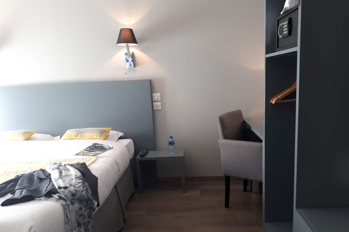 Een hotelkamer met een bed, nachtkastje, lamp, stoel en een kledingkast.