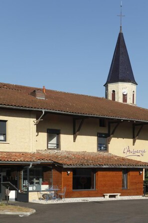 A building with a church steeple, a café named "L'Auberge," and a small outdoor seating area. - Auberge Bressane de Buellas (Buellas)