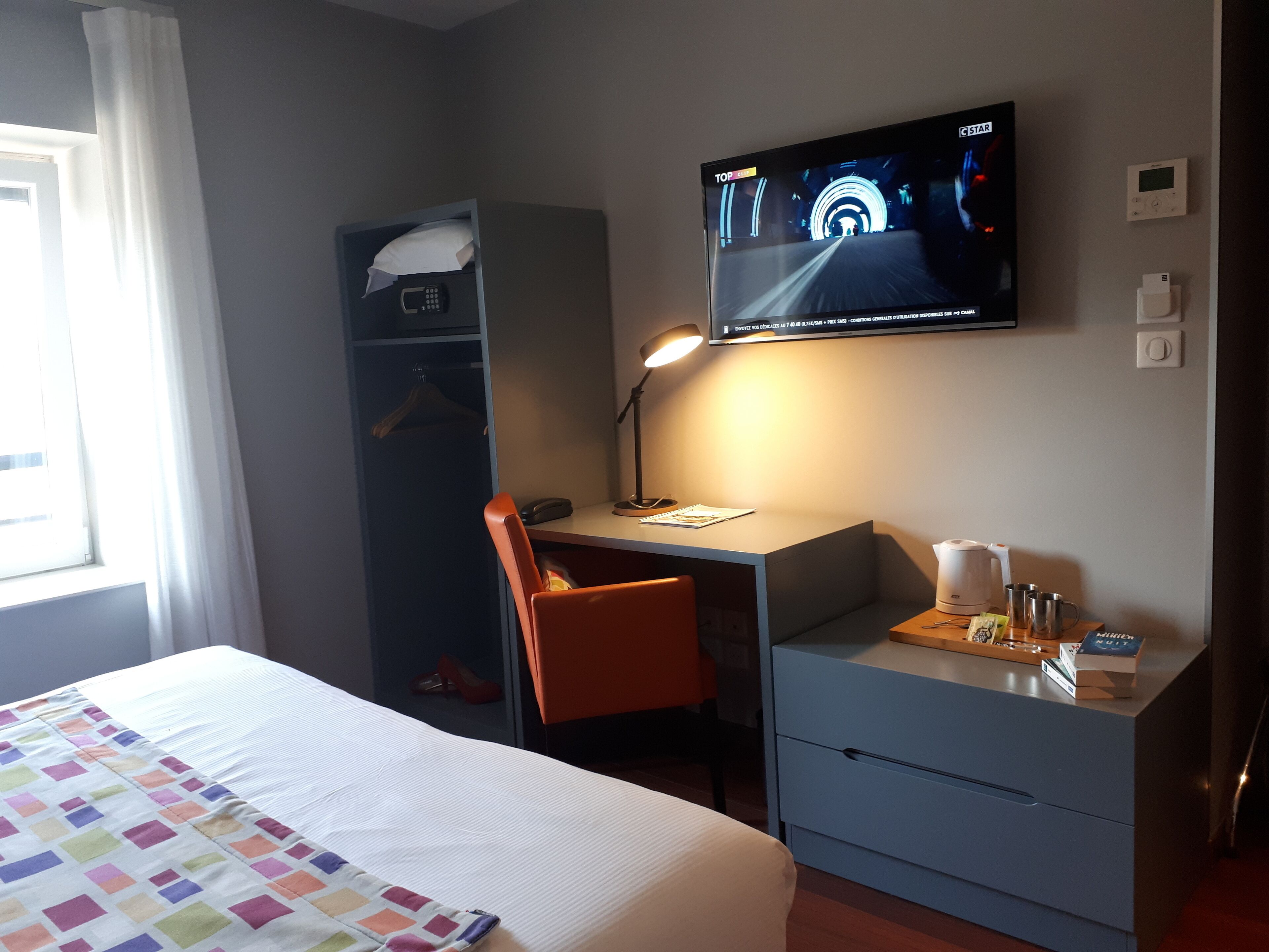 Una habitación de hotel con una cama, un escritorio con silla, un televisor y un armario.