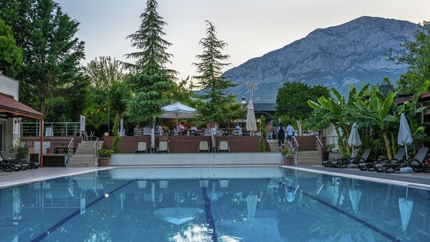 A swimming pool with lounge chairs and umbrellas, surrounded by trees and a mountain in the background. - Rose Resort Hotel (Kemer)
