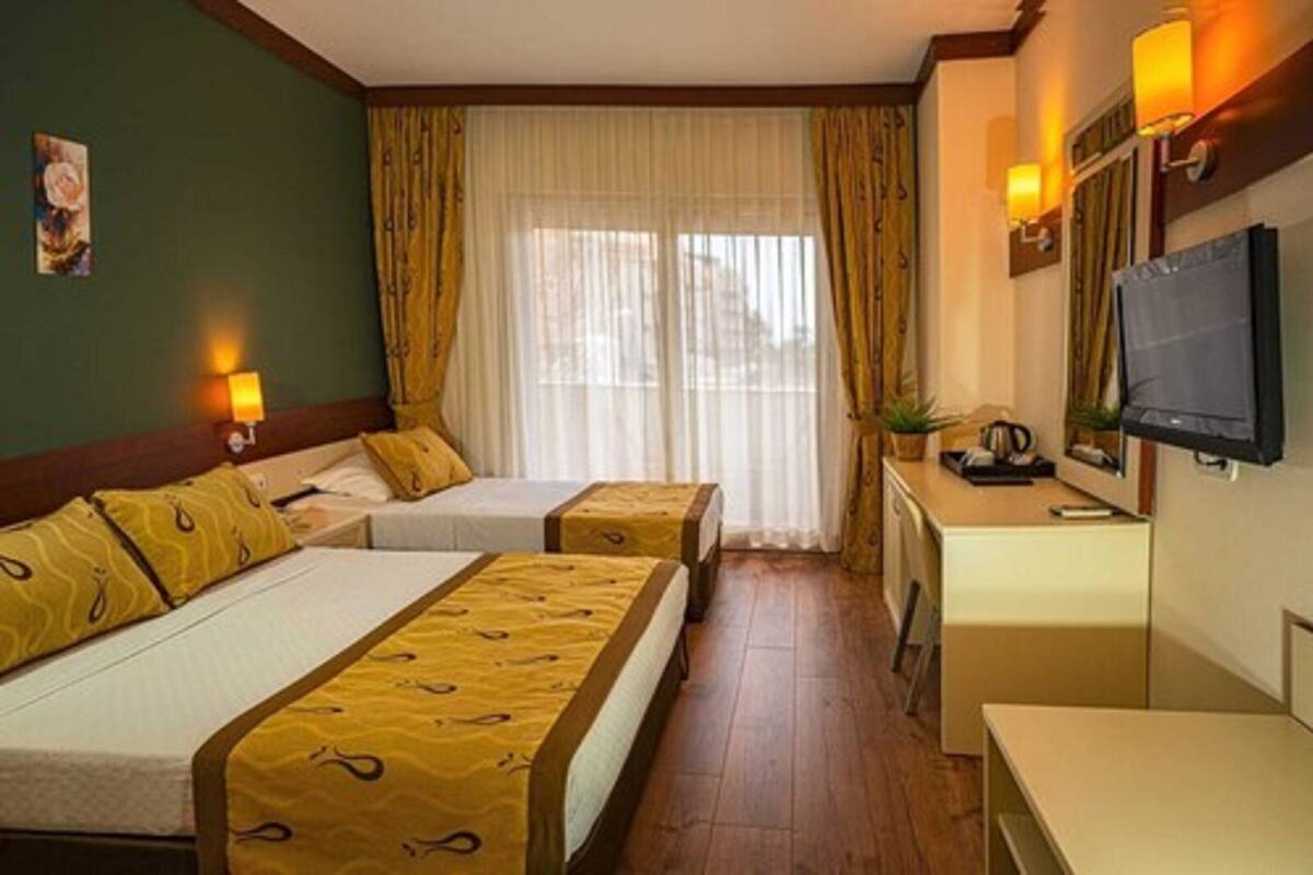 A hotel room with two beds, a desk, a television, and a window with curtains.