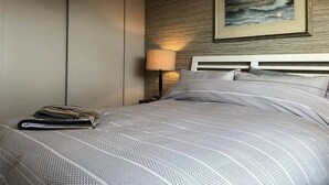 Un lit bien fait, avec une couvre-lit à motifs, une couverture pliée et, au mur, un tableau représentant une mer déchaînée.