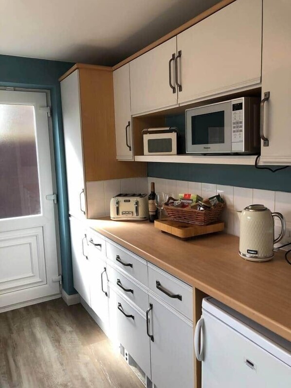 A kitchen with white cabinets, a microwave, a toaster, and a kettle on the counter.