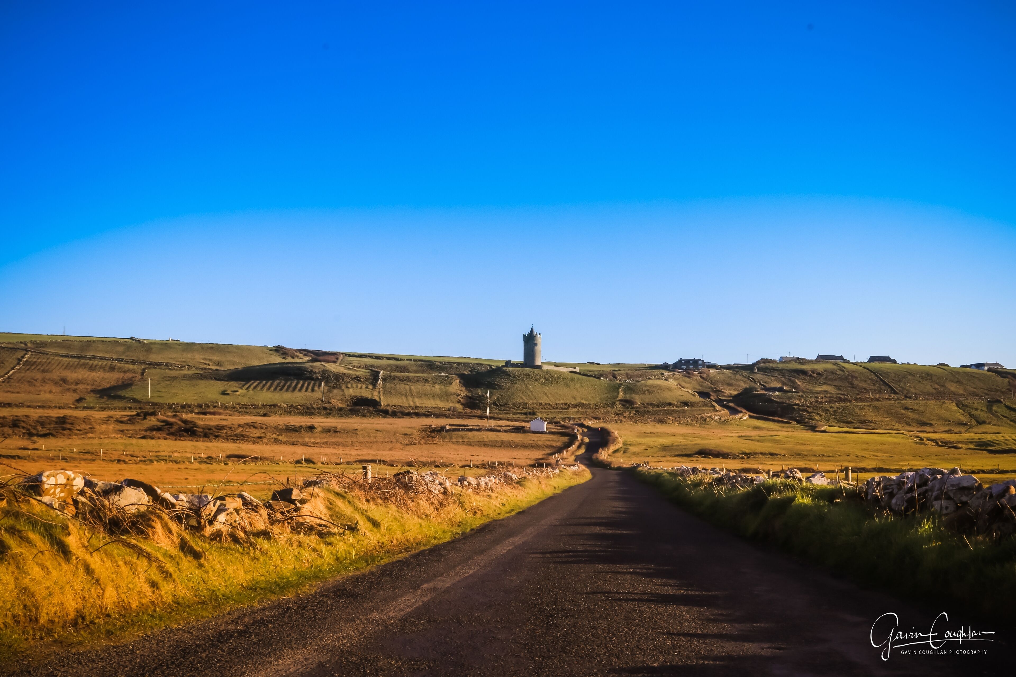 Eine Landstraße führt zu einer turmartigen Struktur in einer hügeligen Landschaft.