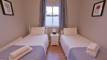 A bedroom with two beds, a nightstand with a lamp, and a window with curtains.