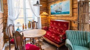 A wooden cabin interior with a round wooden table, red upholstered sofa, and a framed painting of a ship on the wall. - Ibsens B&B (Grimstad)