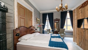 A bedroom with a large bed, a wooden wardrobe, a desk with a chair, a television, and a chandelier. - Ibsens B&B (Grimstad)