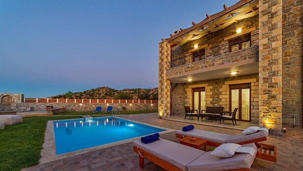 Un espace aménagé au bord de la piscine avec des chaises longues, un bâtiment en pierre doté d’un balcon et une vue dégagée sur le paysage environnant.