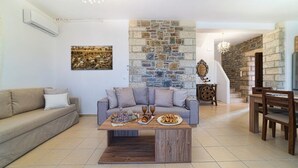 Un salon avec un mur en pierre, un canapé, une table basse avec de la nourriture et un coin repas avec des chaises et une table.