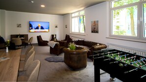 A modern living room with a foosball table, comfortable seating, a television, and large windows. - New Work Hotel Essen (Essen)
