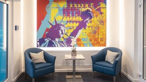 A hallway with two blue armchairs, a small table with a vase, and a colorful mural on the wall. - New Work Hotel Essen (Essen)