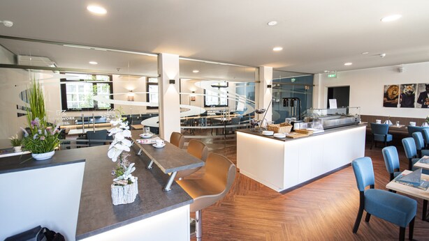 A modern hotel restaurant with a central island, seating areas, and a view of the hotel lobby. - New Work Hotel Essen (Essen)