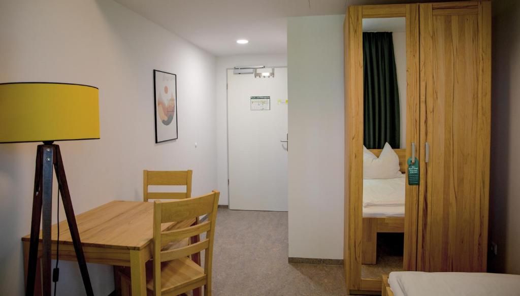 A room with a wooden table, chairs, a bed with a wooden headboard, a lamp, and a door leading to another room.