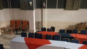 A conference room with tables covered in white and red tablecloths, arranged in rows. - Amity Hotel (Gilgil)