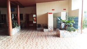 A covered outdoor area with tiled flooring, potted plants, and a sign indicating a washroom. - The Delta Falls Hotel (Nyahururu)