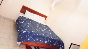 A small, simple room with a bed, a wooden headboard, and a plain wall. - The Delta Falls Hotel (Nyahururu)