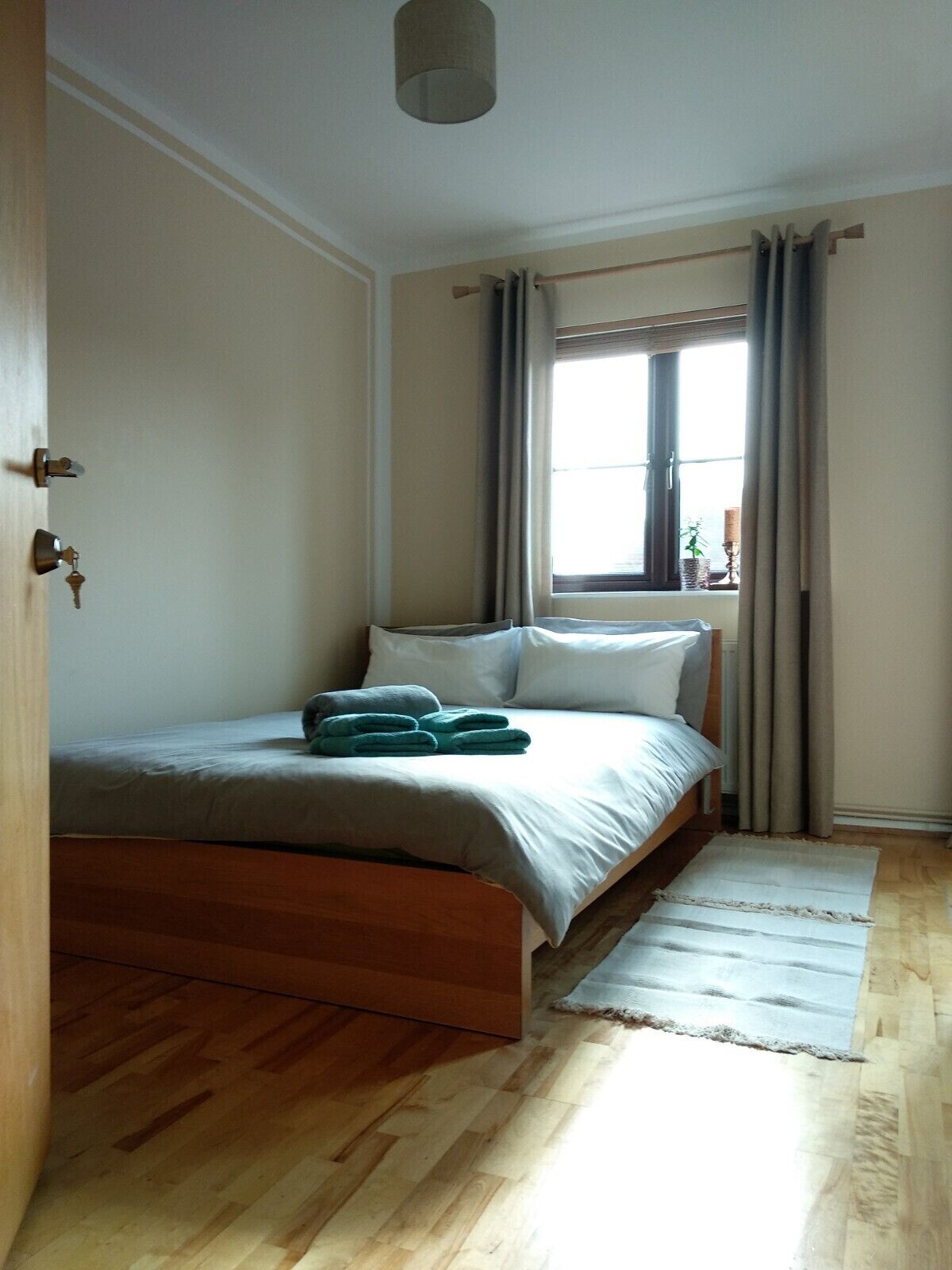A bedroom with a wooden bed, a window with curtains, and a view of the outside.
