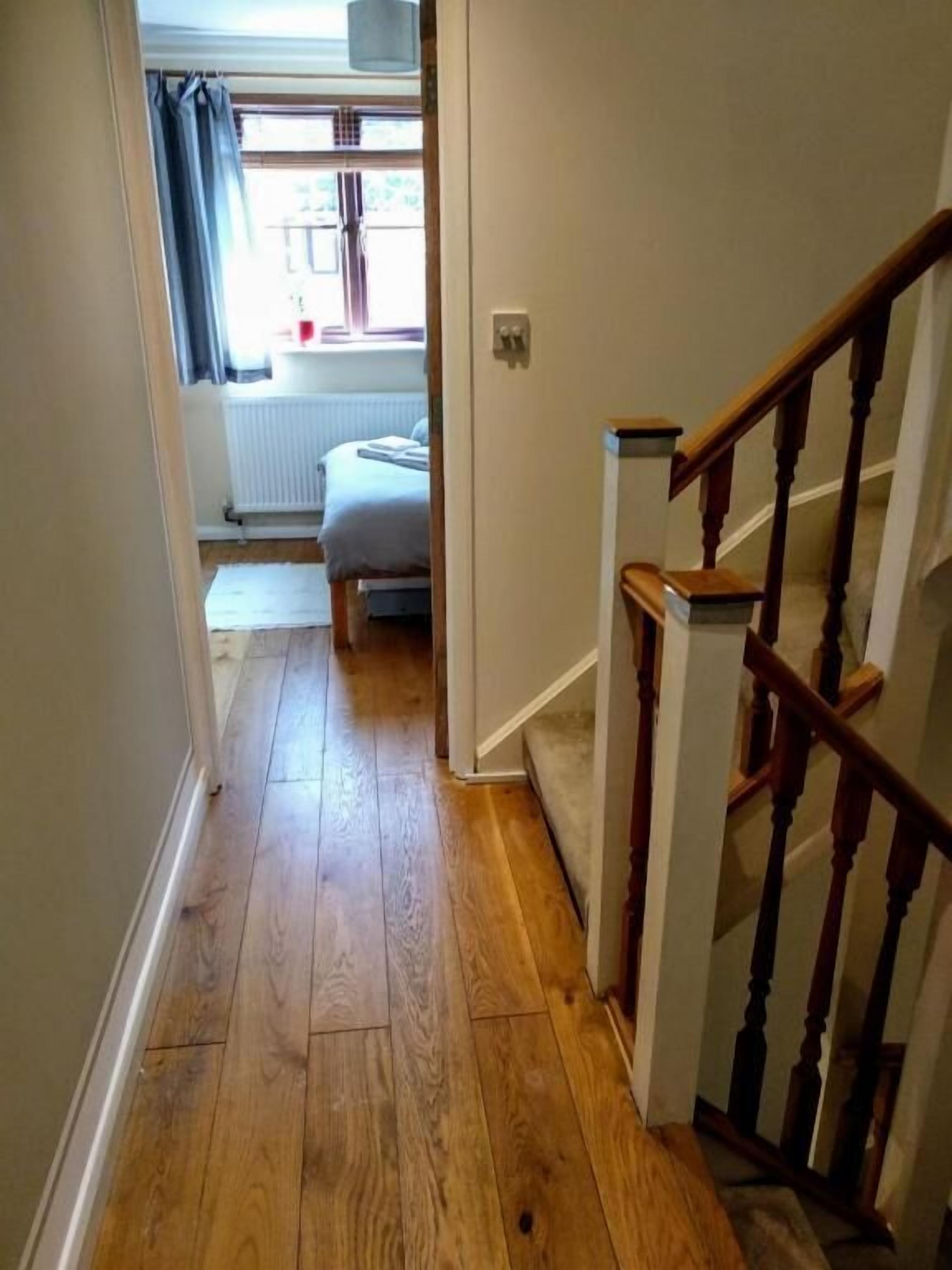 A hallway with wooden flooring leading to a bedroom with a bed and a radiator.
