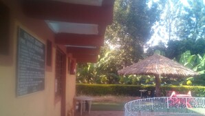 A pool area with a metal fence, a thatched umbrella, and a signboard on a building. - Sun Citi Resort (Sagana)