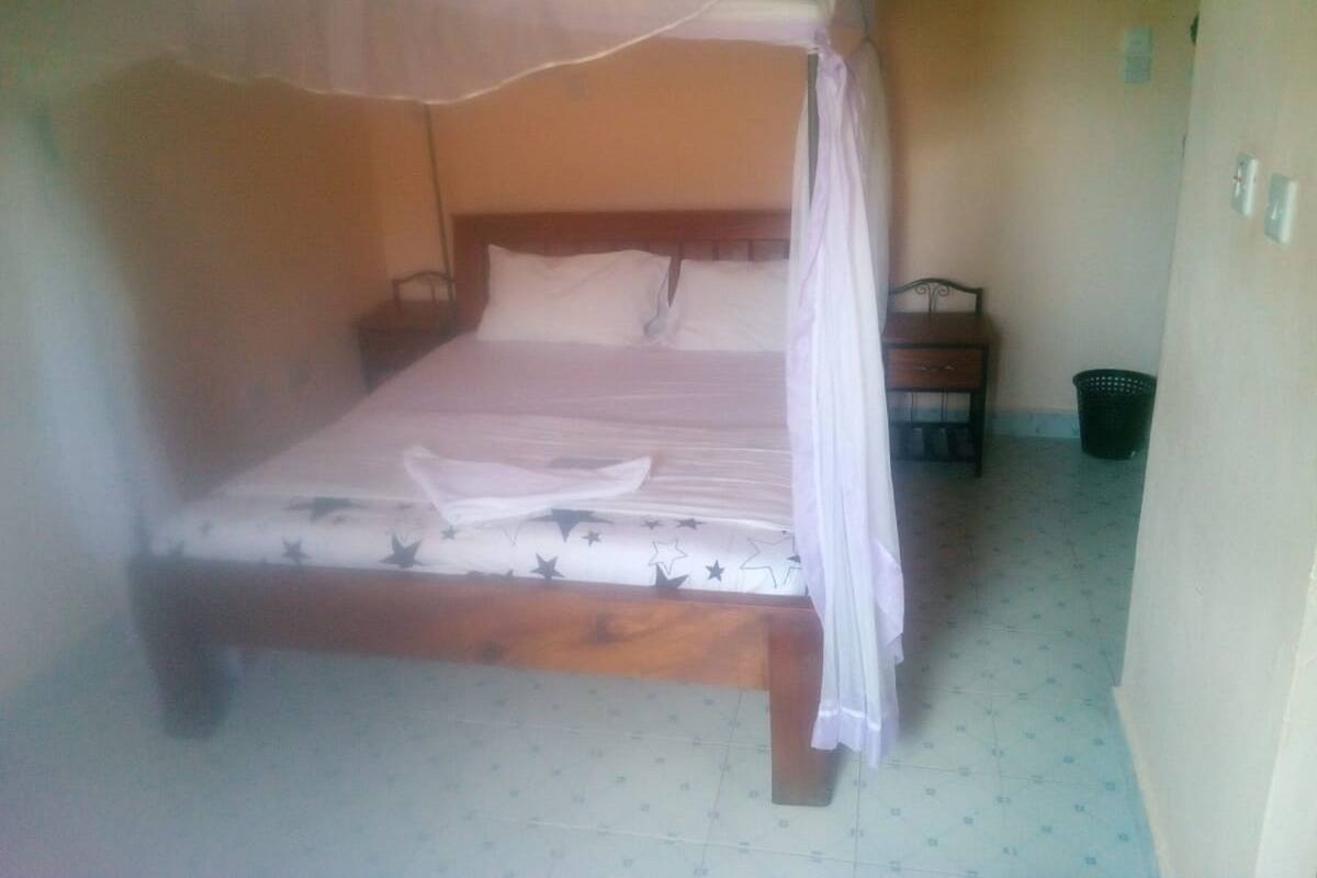 A single bed with a canopy, a nightstand, and a trash bin in a room with patterned flooring.