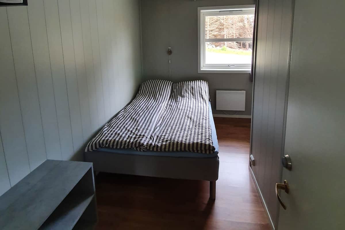 Una habitación pequeña con cama individual, ventana, radiador y ventilador de techo.