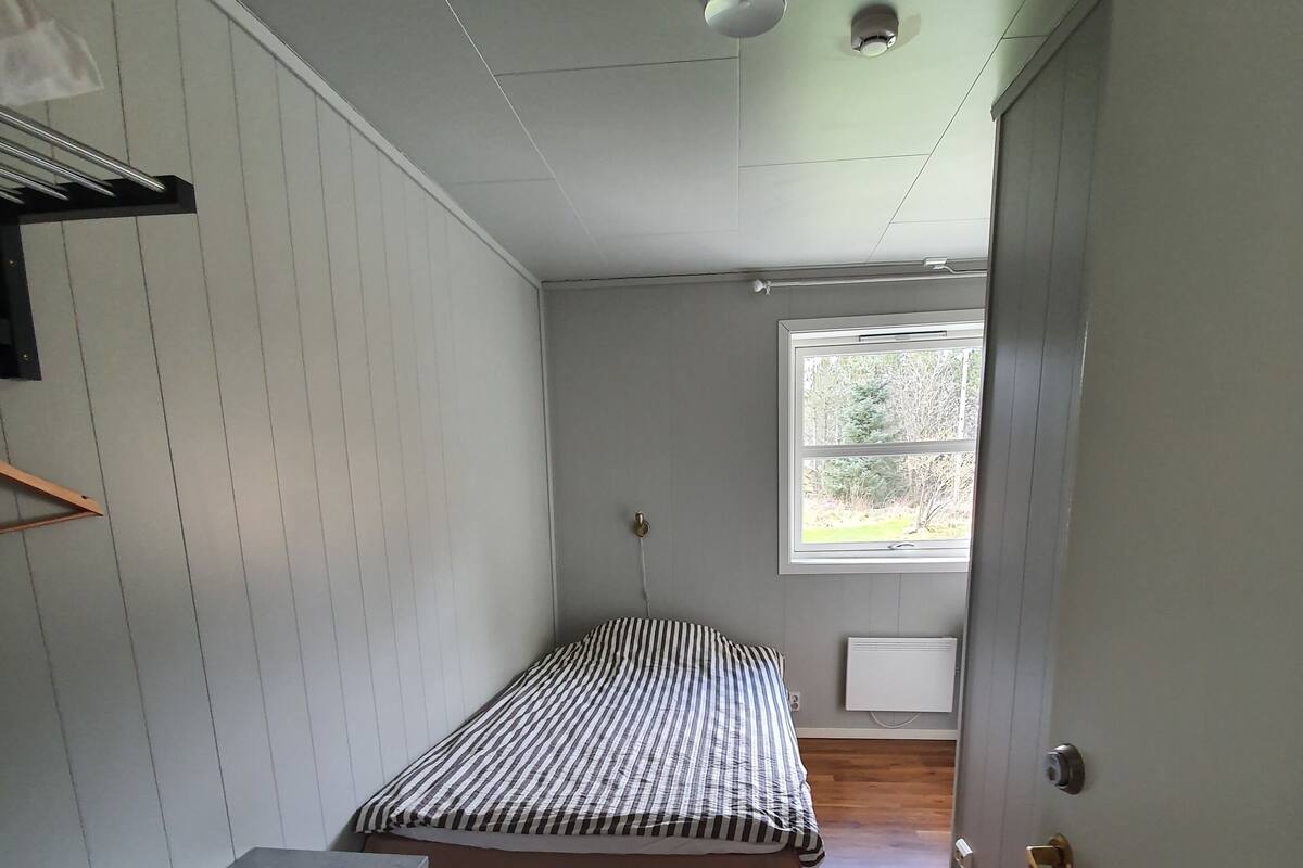 Un dormitorio compacto con una cama, un escritorio pequeño y una ventana que ofrece vistas al exterior.