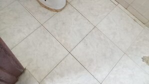 Eine Toilette in einem Badezimmer mit Fliesenboden und einer sichtbaren Rohrleitung an der Wand.