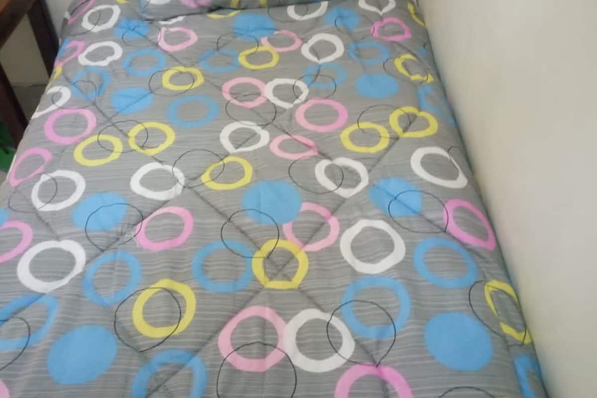 A single bed with a grey bedspread featuring a multicolored circular pattern.