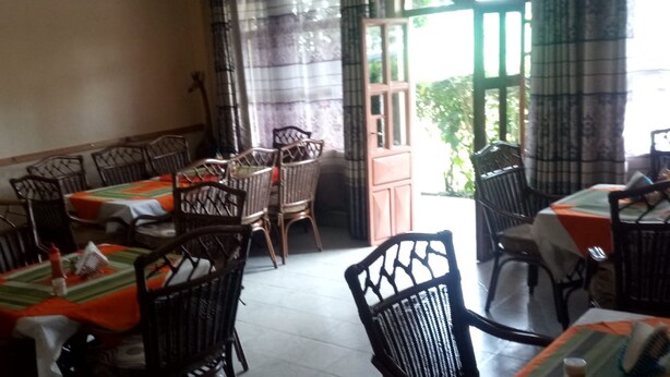 A dining area with tables and chairs, large windows, and a view of greenery outside. - Chawaka Guest House (Gilgil)