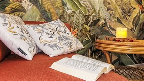 Quarto com tapete vermelho, mesinha de madeira com uma vela acesa, um livro e almofadas decorativas com estampas de animais.