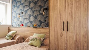 Quarto com duas camas, guarda-roupa de madeira e parede com papel de parede estampado com folhas.
