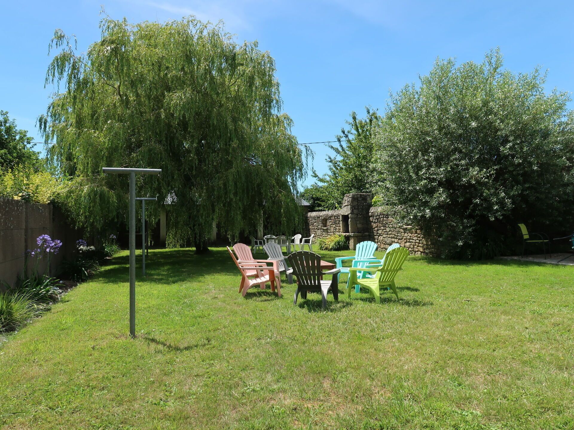 Ein Garten mit einer Steinmauer, einem Holztisch und mehreren Adirondack-Stühlen.