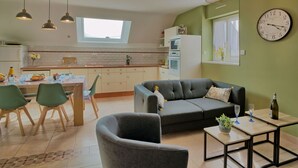 A modern living room with a grey sofa, a dining area with a table and chairs, a kitchen with white cabinets, and a large window. - Nice apartment in villa for 5 people with WIFI, TV and terrace (Le Magouër)