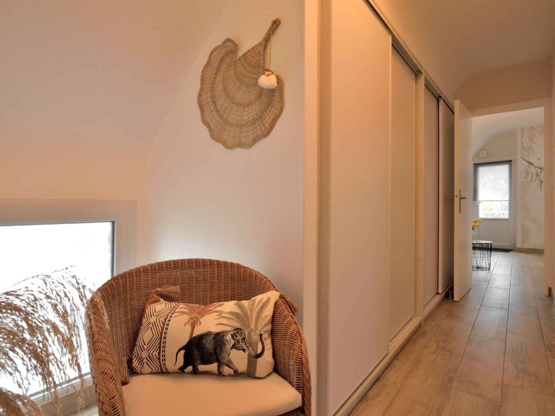 Ein modernes Interieur mit einem Korbssessel, einer Wanddekoration und Blick in einen Essbereich.