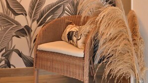 A wicker chair with a cushion in front of a wall with a tropical leaf pattern.